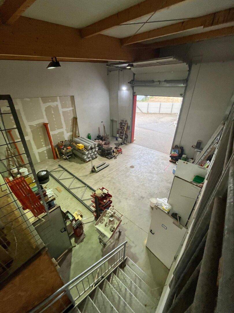 Blick von oben in eine Lagerhalle mit Betonboden, Trockenbauwänden und einem geöffneten Rolltor.
