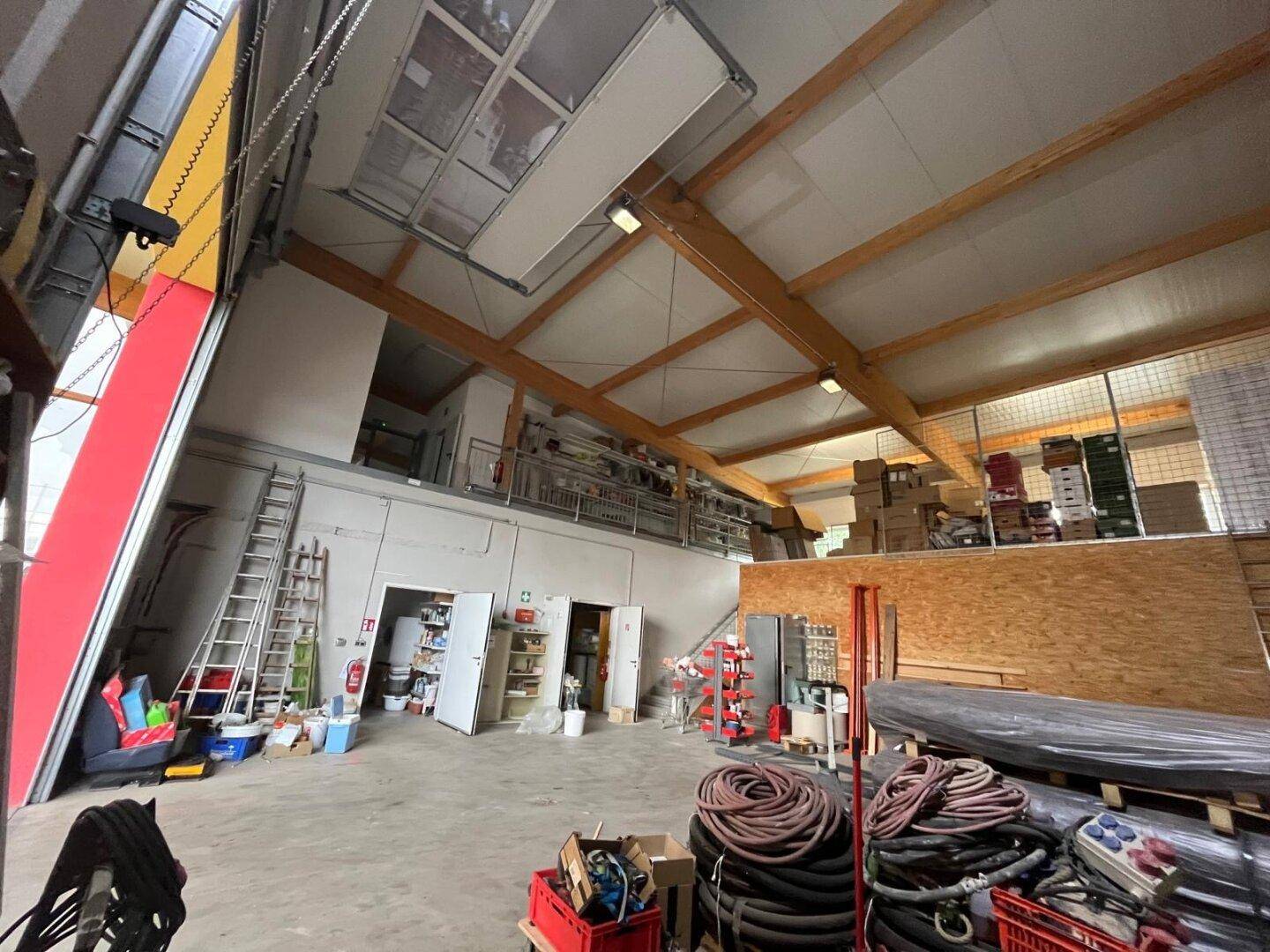 Innenansicht einer Lagerhalle mit großem Rolltor, hohen Decken und sichtbaren Holzbalken, sehr geräumig.