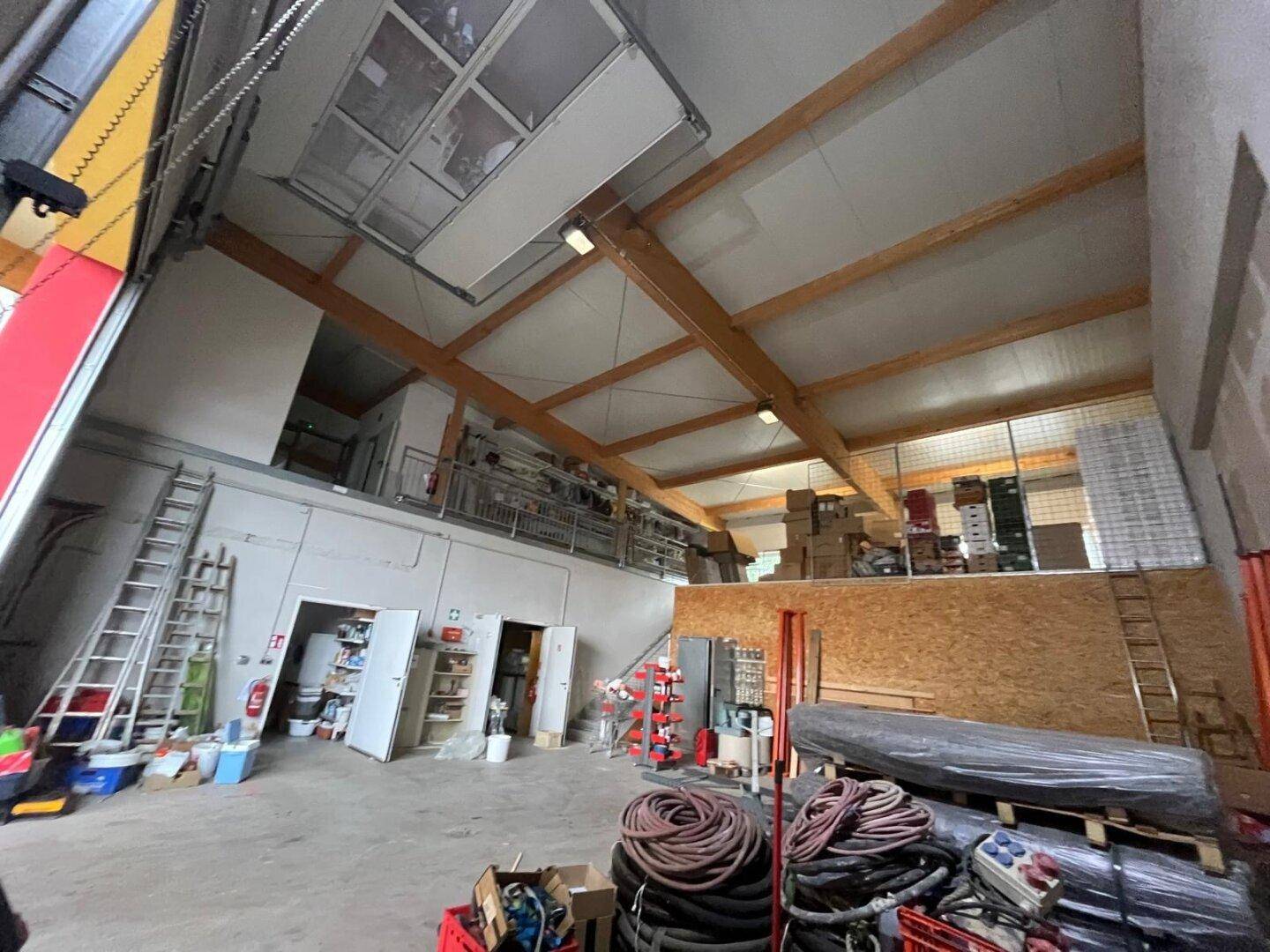 Geräumige Lagerhalle mit hohen Decken, Holzbalken und einem großen Rolltor, ideal für Betrieb und Lagerung.