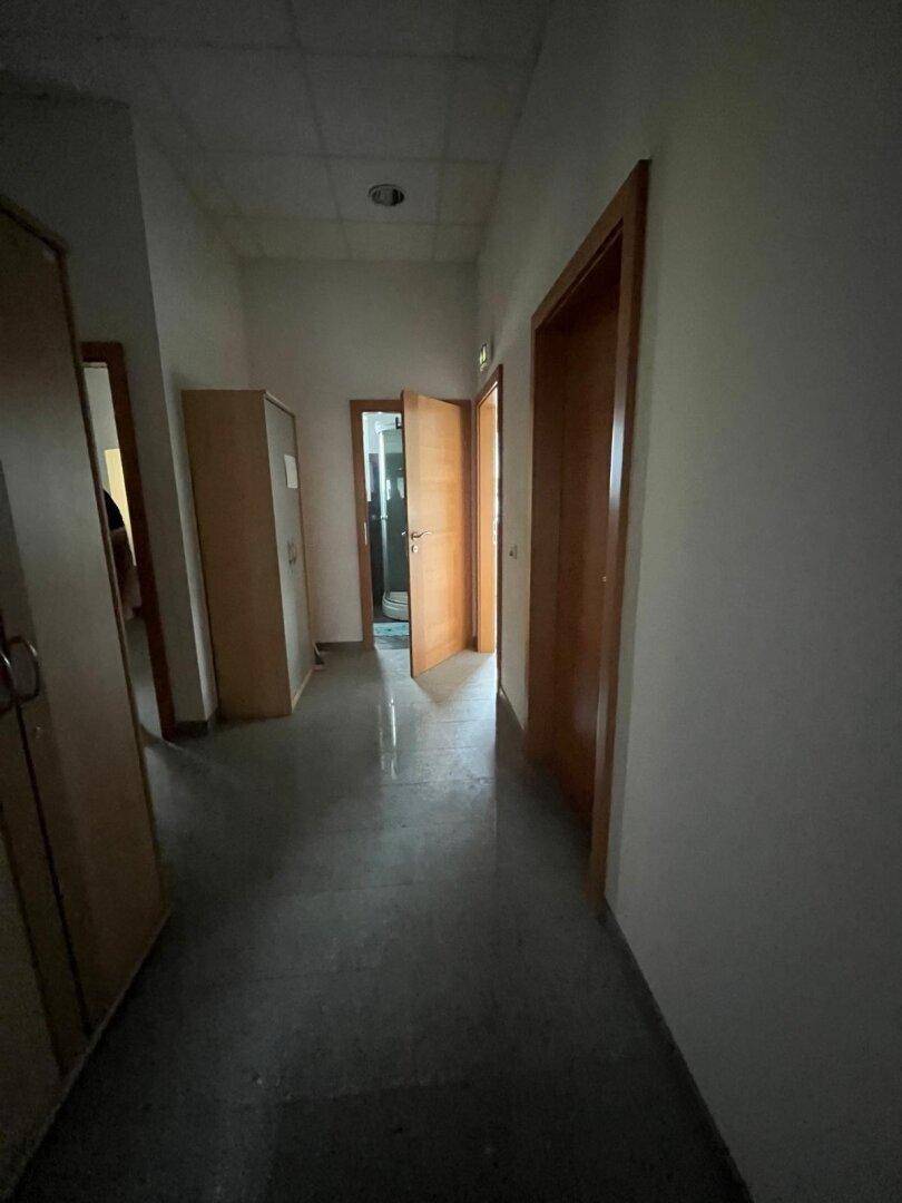 Langer Flur mit dunklem Fliesenboden, hellen Wänden und mehreren Holztüren.