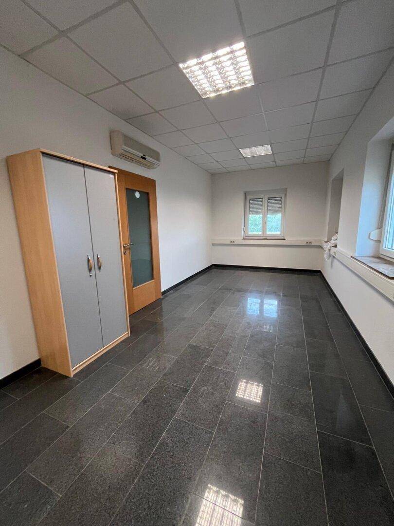 Leeres Büro mit dunklem Fliesenboden, weißen Wänden, Fenster und einer Klimaanlage.