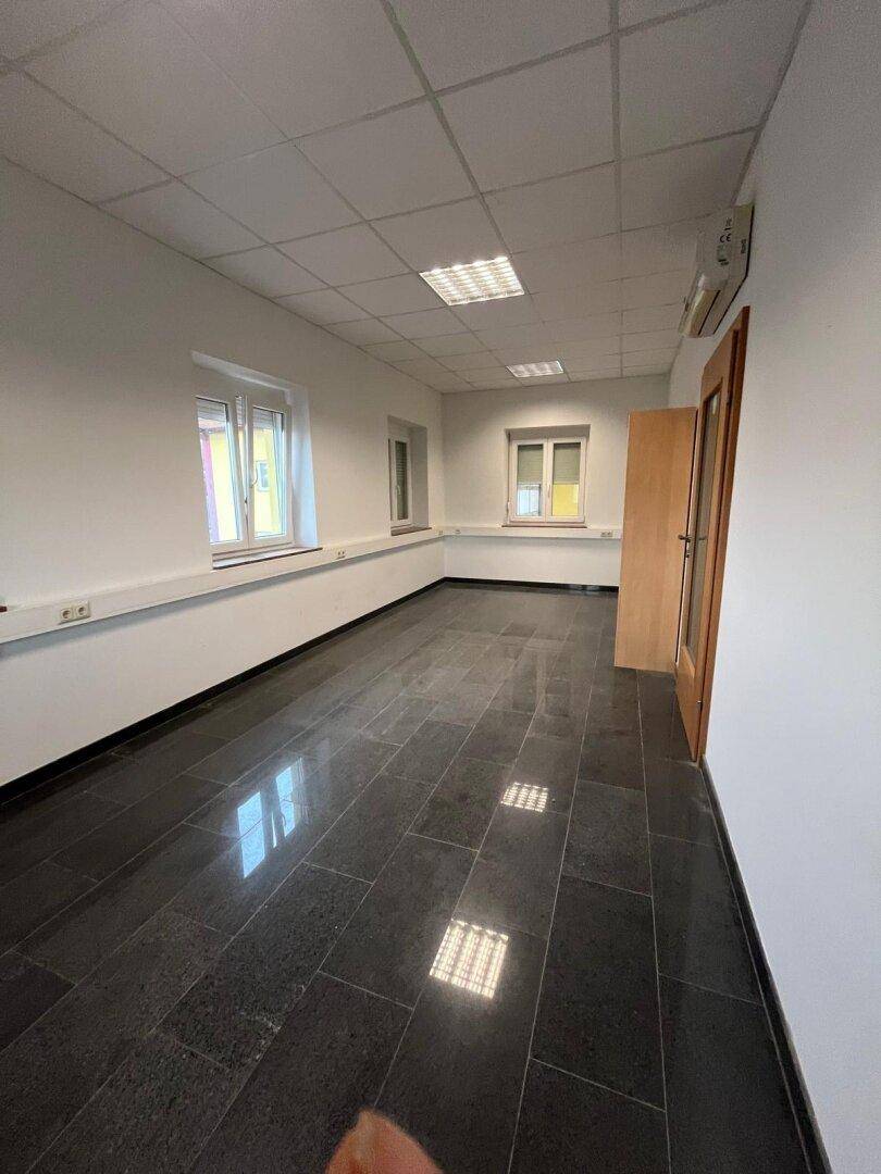 Helles und geräumiges Büro mit dunklem Fliesenboden, weißen Wänden und mehreren Fenstern.