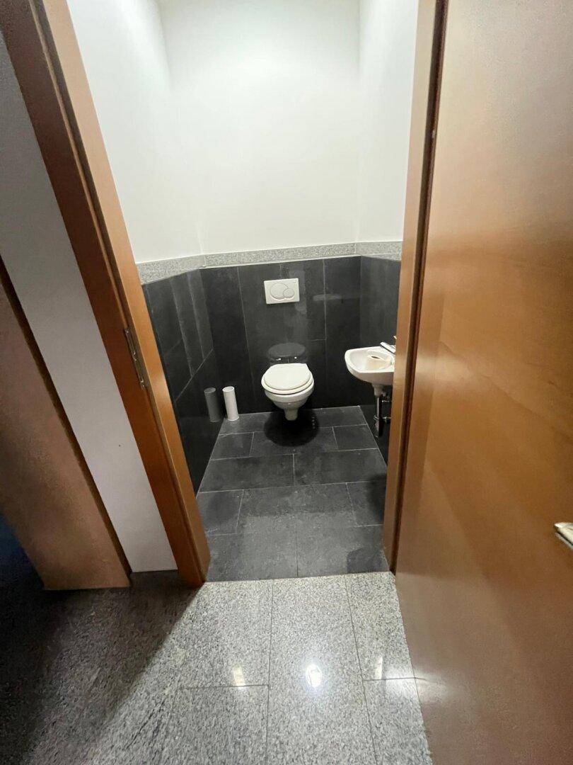 Kleines Gäste-WC mit dunklen Fliesen an Wand und Boden sowie einem einfachen Waschbecken.