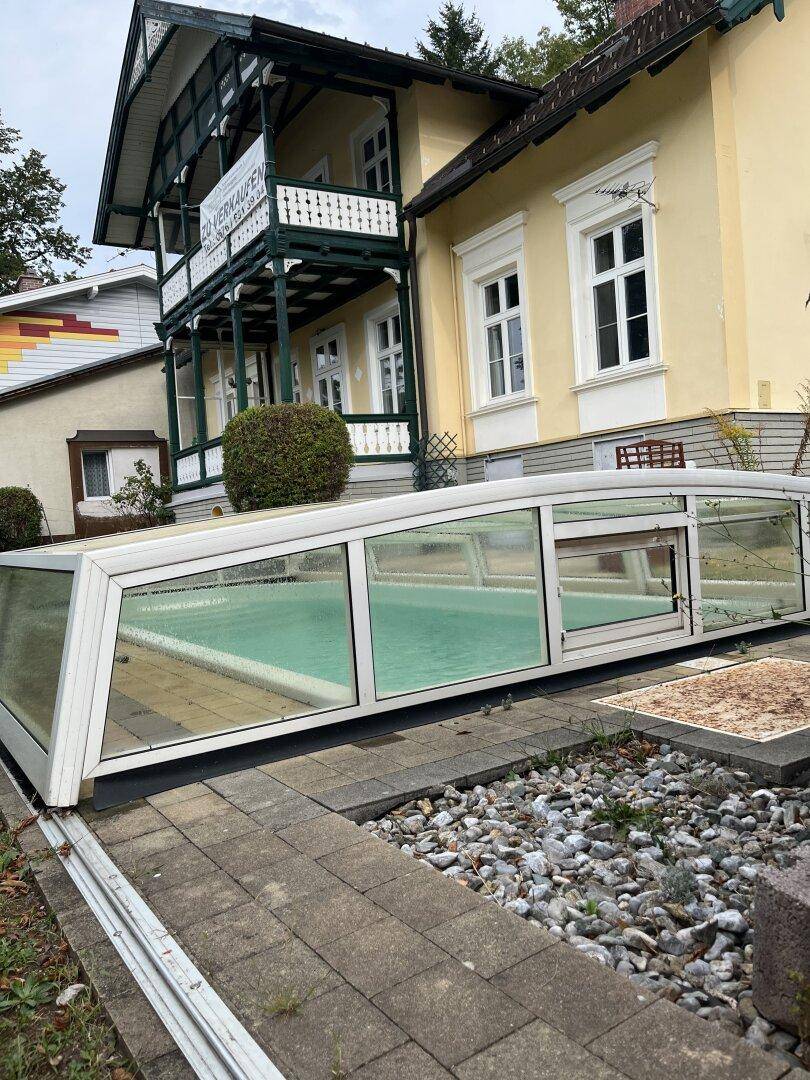 Überdachter Swimmingpool im Gartenbereich vor der historischen Hausfassade.