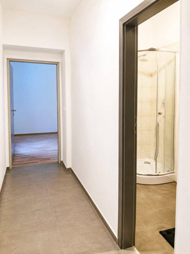Heller Flur mit Fliesenboden und Zugang zu einem Badezimmer mit Duschkabine.
