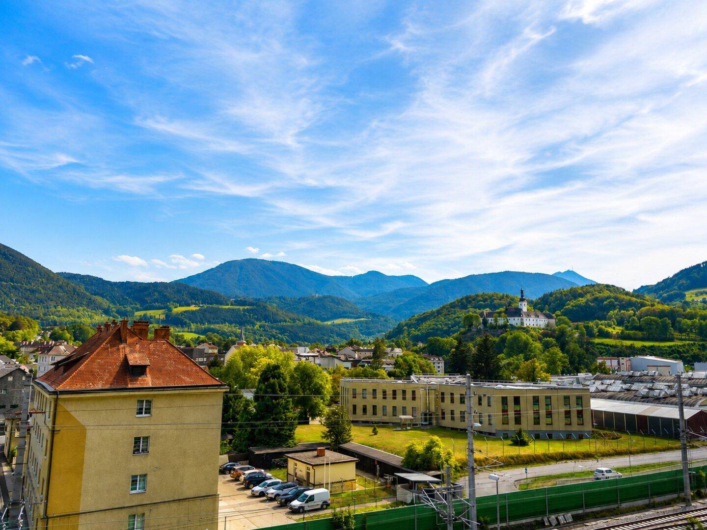 Aussicht auf eine Stadt mit historischen Gebäuden und einem Kloster auf einem Hügel vor einer Bergkulisse.