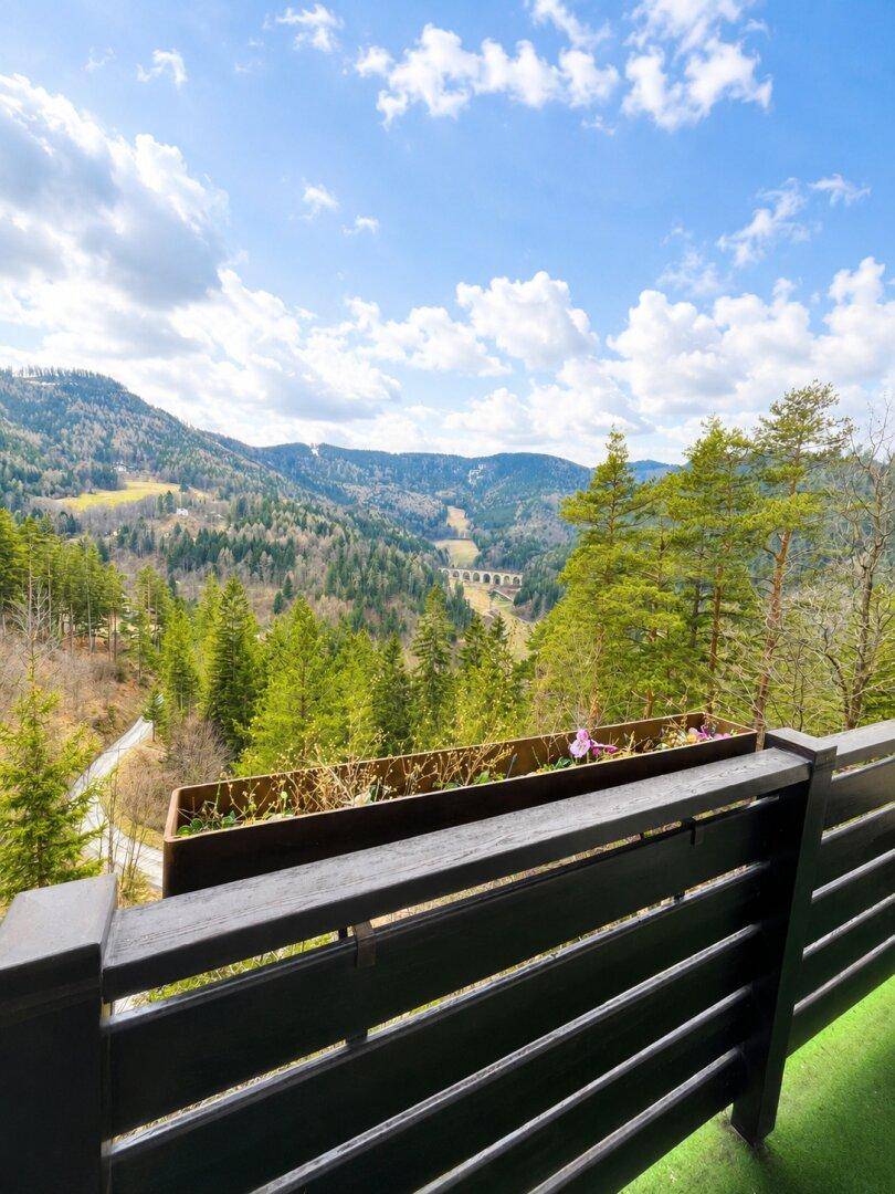 Weitblick von einem Balkon über eine bewaldete Berglandschaft mit einem Viadukt in der Ferne.