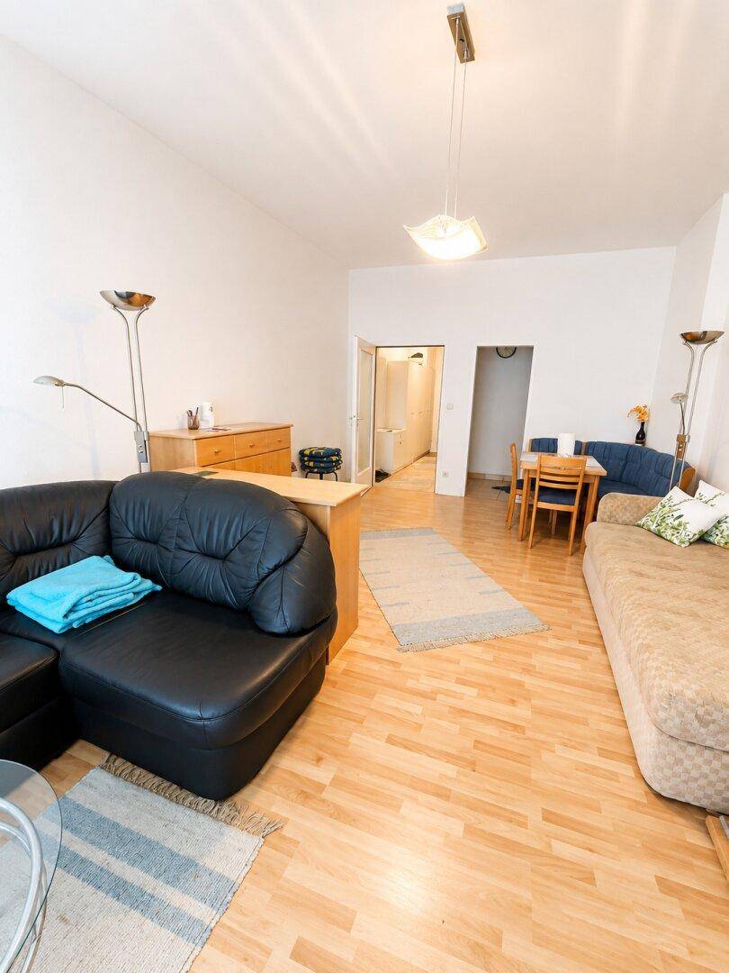 Helles Wohn-Esszimmer mit schwarzem Ecksofa, Tagesbett und hellem Laminatboden.