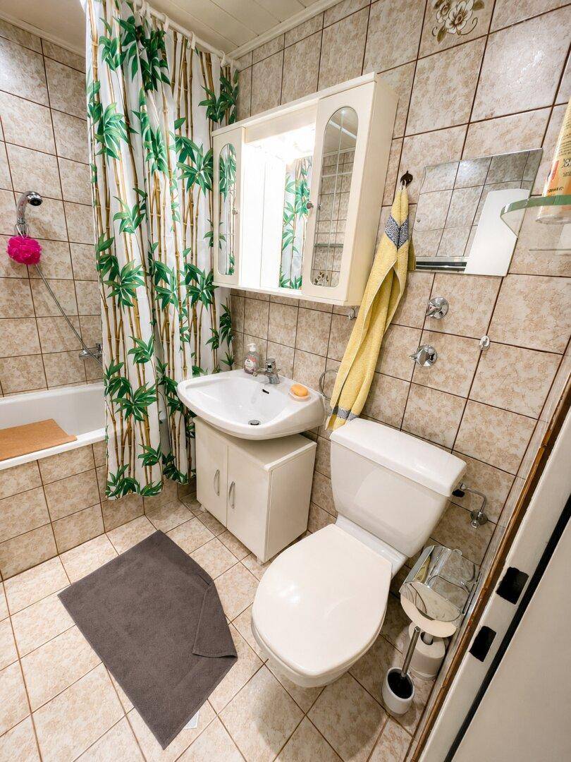 Gefliestes Badezimmer mit Badewanne, WC, Waschbecken und einem Spiegelschrank.