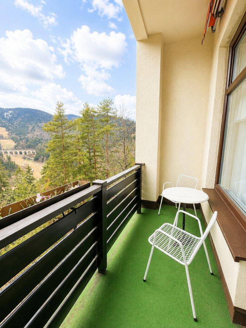 Möblierter Balkon mit Sitzgelegenheiten und weitem Blick über eine grüne Berglandschaft.