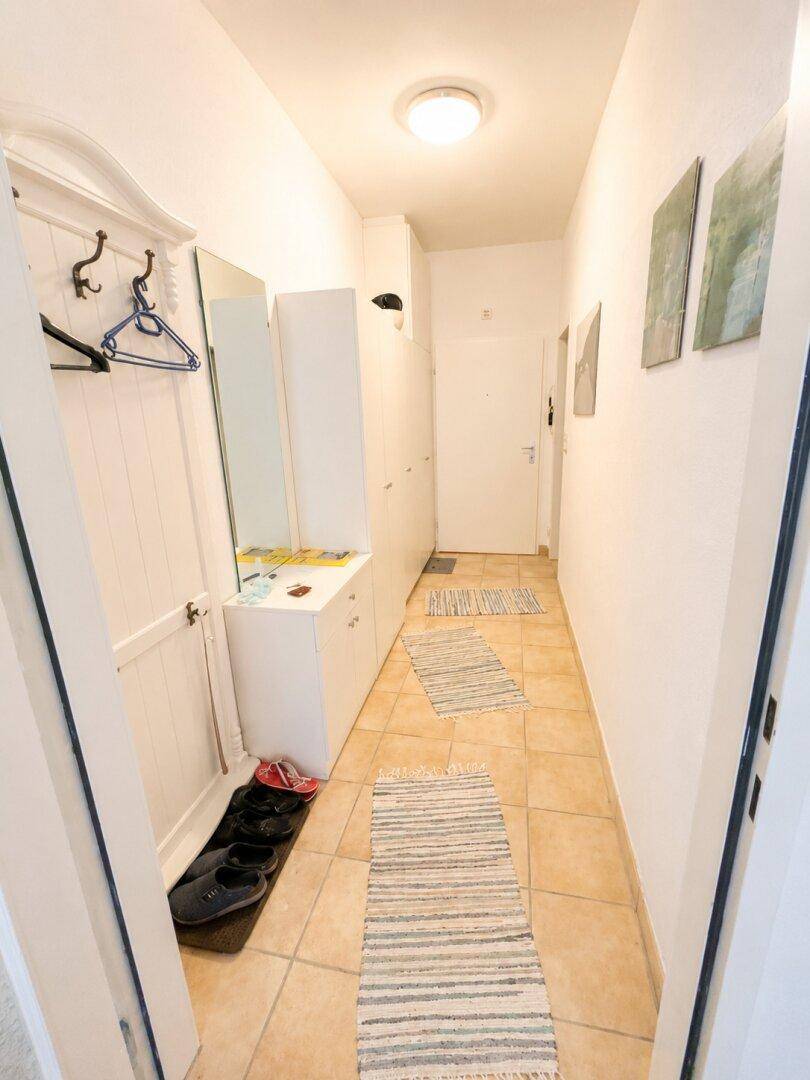 Heller Flur mit Fliesenboden, Garderobe und einem Spiegelschrank am Eingangsbereich.