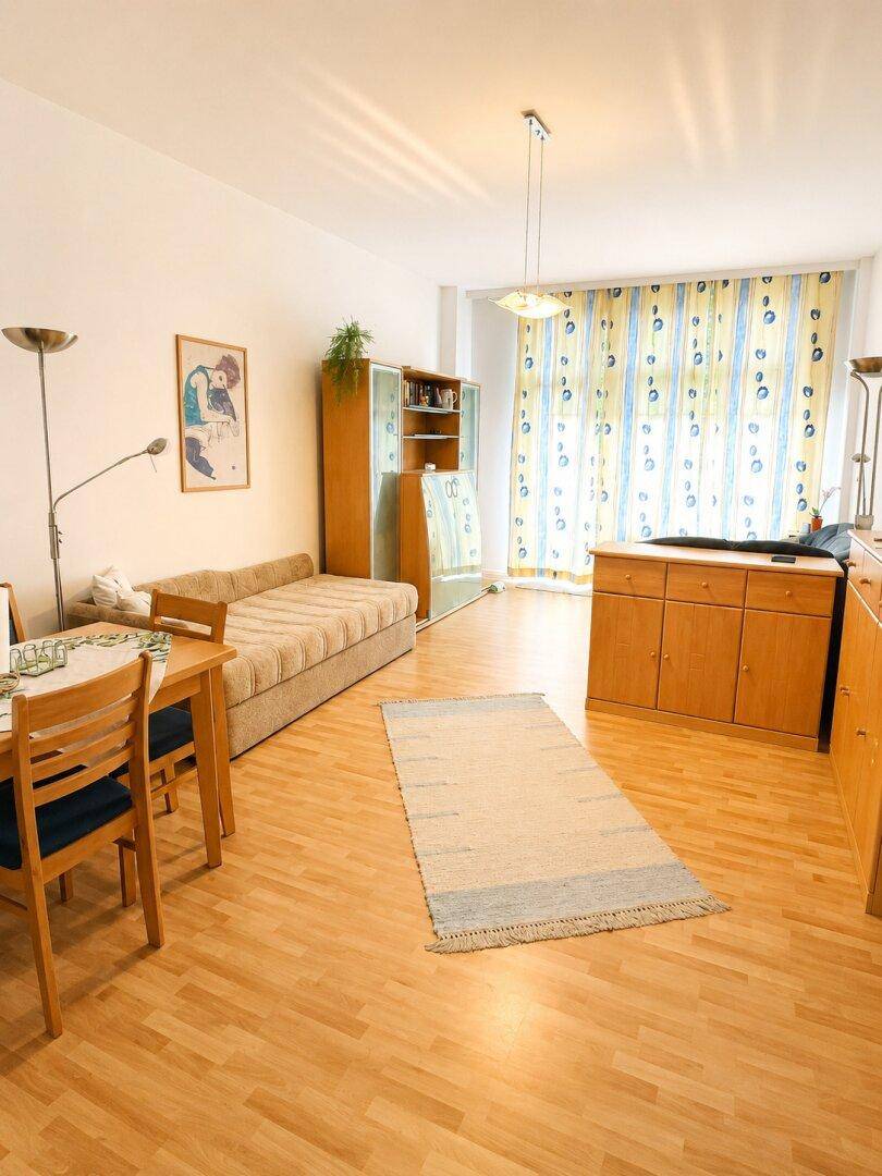 Gemütlicher Wohnbereich mit Tagesbett, Esstisch und hellen Holzmöbeln auf Laminatboden.