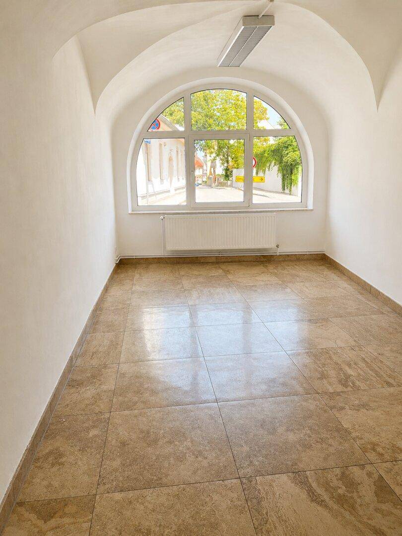 Heller Raum mit großem Rundbogenfenster, Heizkörper und gewölbter Decke, ideal für verschiedene Nutzungen.