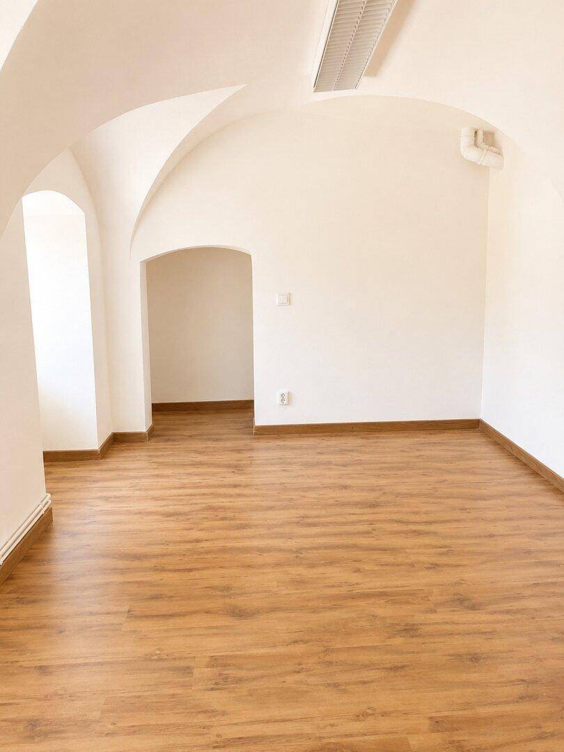 Leerer Raum mit gewölbter Decke und Laminatboden, der durch einen Bogen mit einem weiteren Bereich verbunden ist.