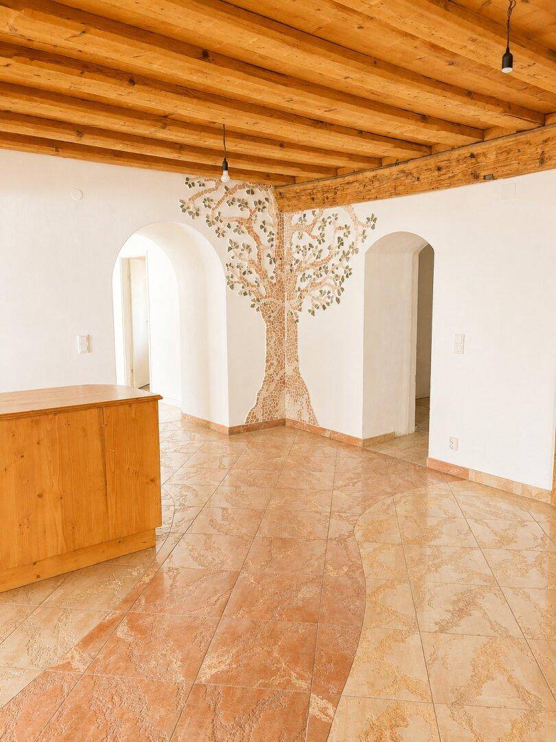 Geräumiger Wohnbereich mit Holzbalkendecke, dekorativem Fliesenboden und einem Mosaikbaum an der Wand.