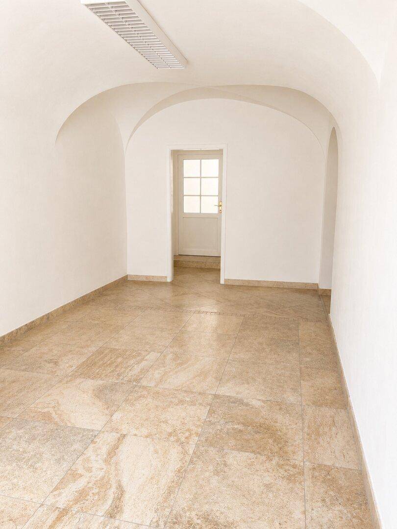 Langer Flur mit gewölbter Decke und Fliesenboden, der zu einer Tür mit Glasausschnitten führt.