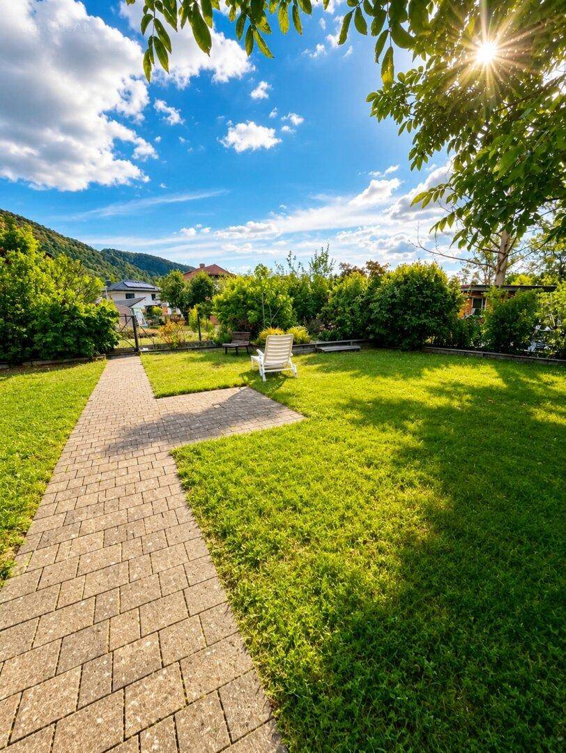 Gepflasterter Gartenweg führt durch die grüne Rasenfläche mit Weitblick auf die Landschaft.