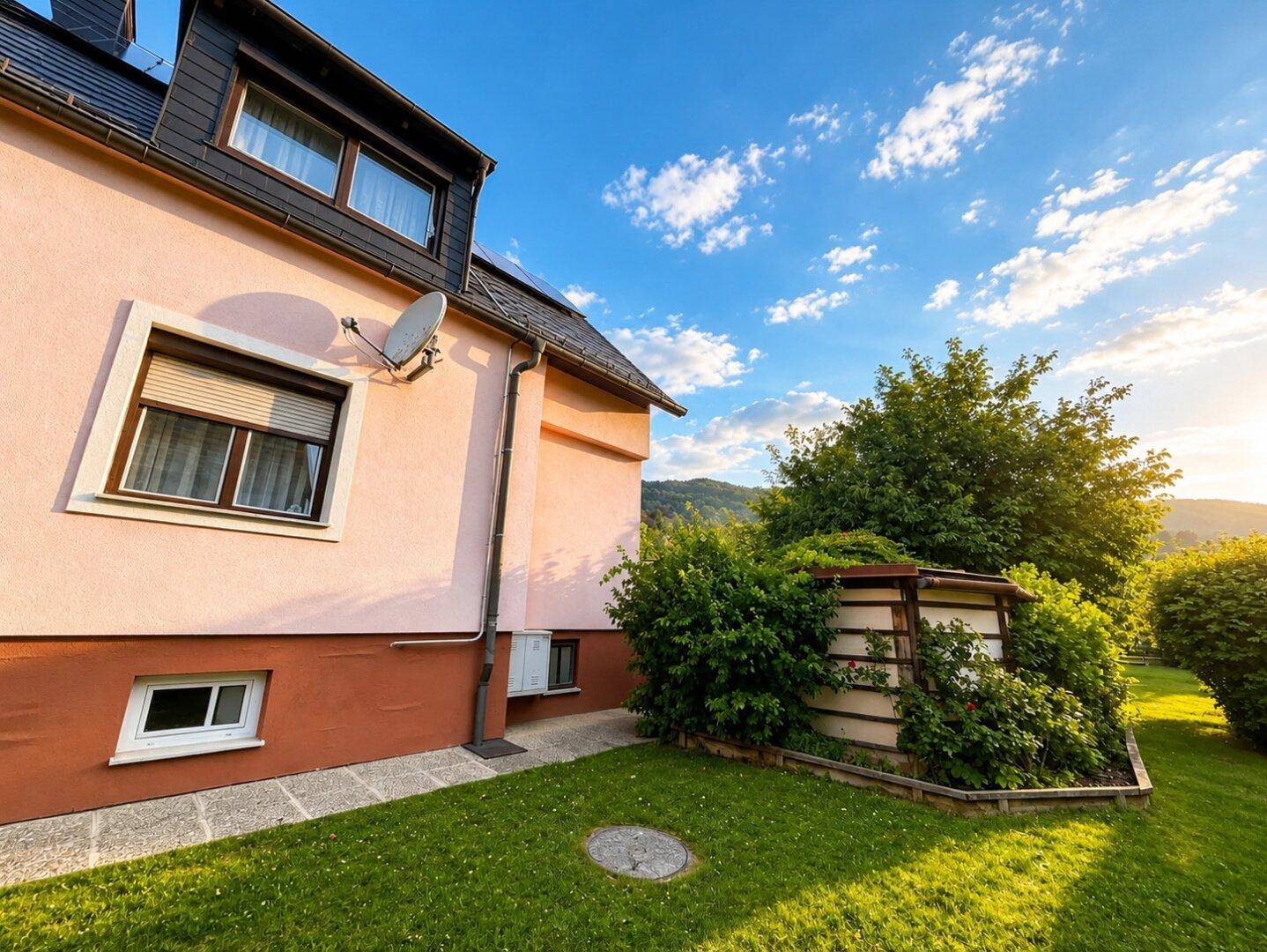 Seitenansicht des Hauses mit grünem Rasen und Büschen im Gartenbereich bei Sonnenschein.