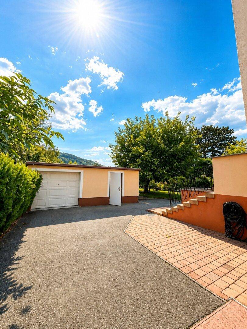 Einfahrt zum Haus mit Garage und Außentreppe unter strahlend blauem Himmel.
