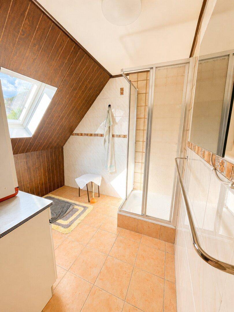 Badezimmer im Dachgeschoss mit Duschkabine, Fliesenboden und Dachfenster.