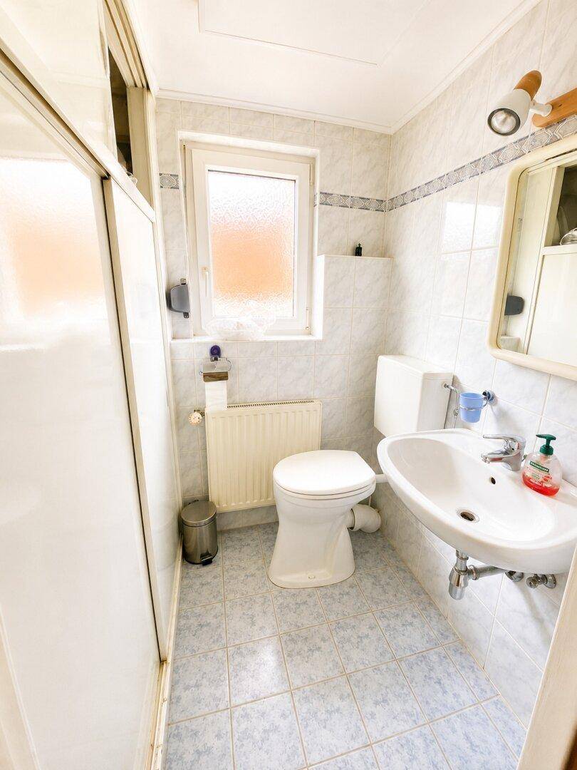 Helles Badezimmer mit Duschkabine, WC, Waschbecken und Fenster.