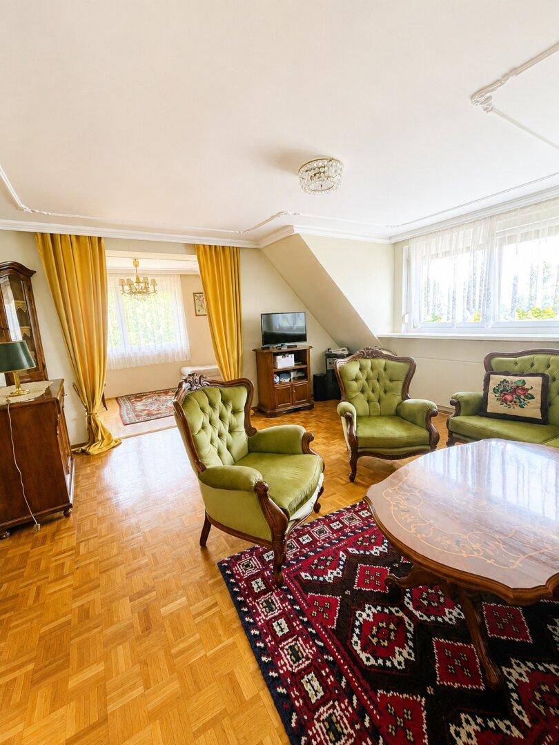Traditionelles Wohnzimmer mit Parkettboden, grünen Sesseln und opulenten Vorhängen.