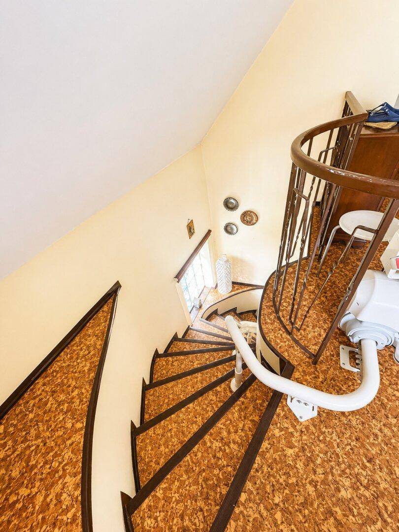 Wendeltreppe mit Treppenlift und gemustertem Bodenbelag für Barrierefreiheit.
