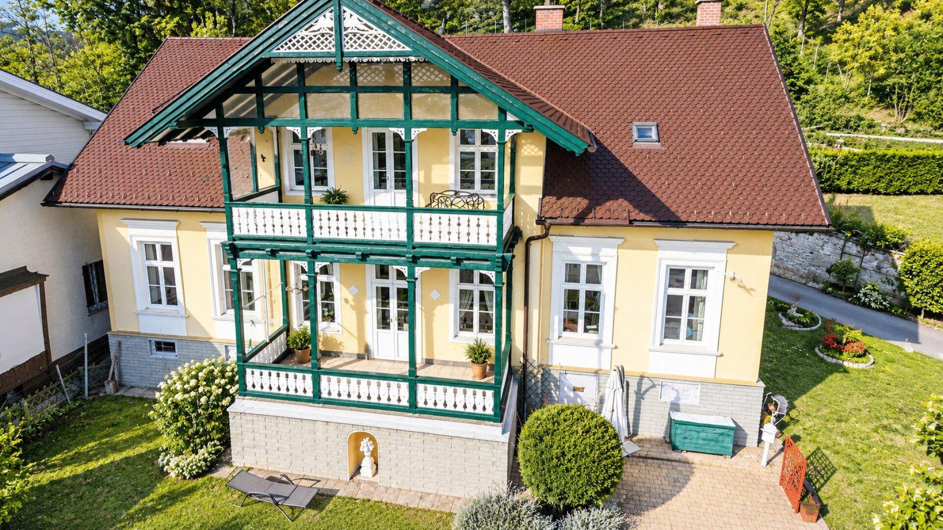 Vorderansicht eines charmanten Hauses mit gelber Fassade, grünen Balkonen und einem gepflegten Vorgarten.