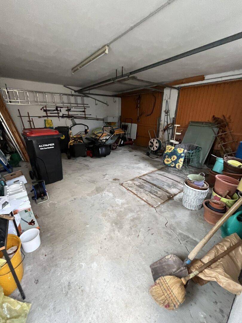 Innenansicht einer Garage, gefüllt mit Werkzeugen, Mülleimern und Gartengeräten.