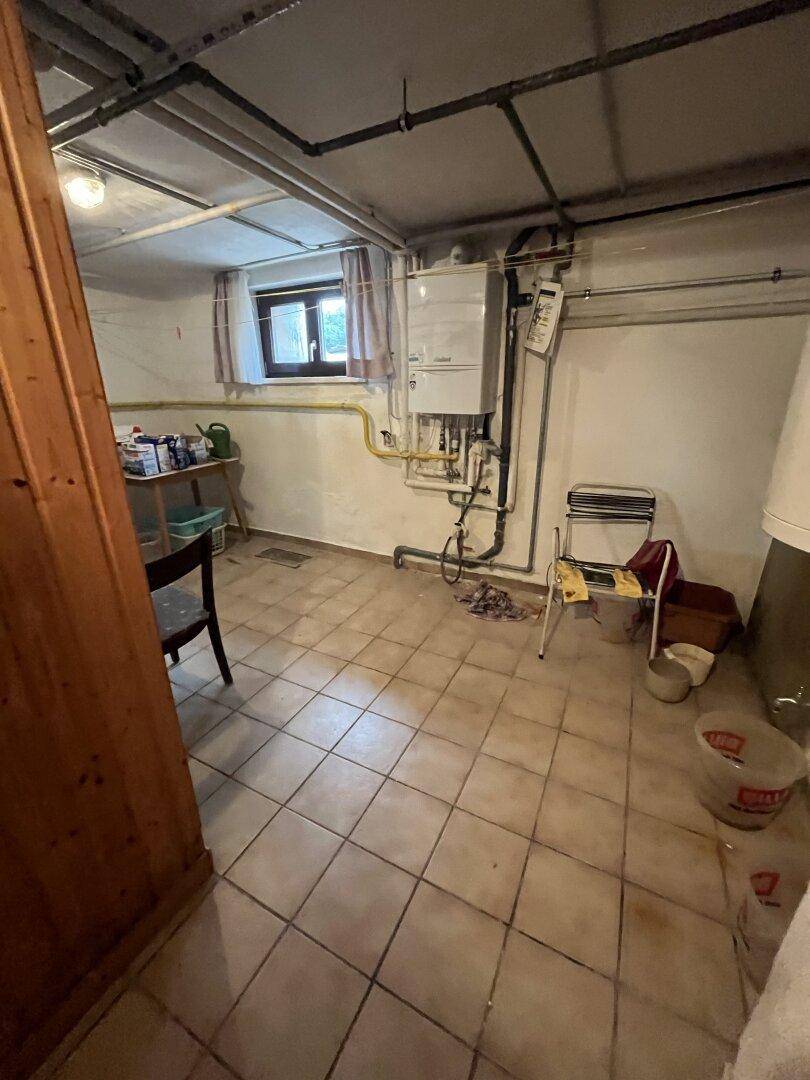 Kellerraum mit Heizungsanlage, sichtbaren Rohren und Fliesenboden, dient als Technikraum.