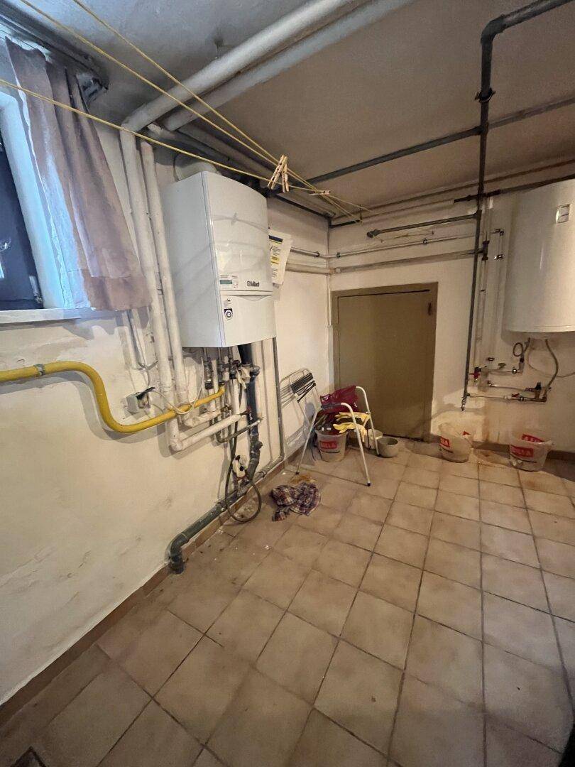 Heizungsraum im Keller mit Gastherme, sichtbaren Rohren und Fliesenboden.