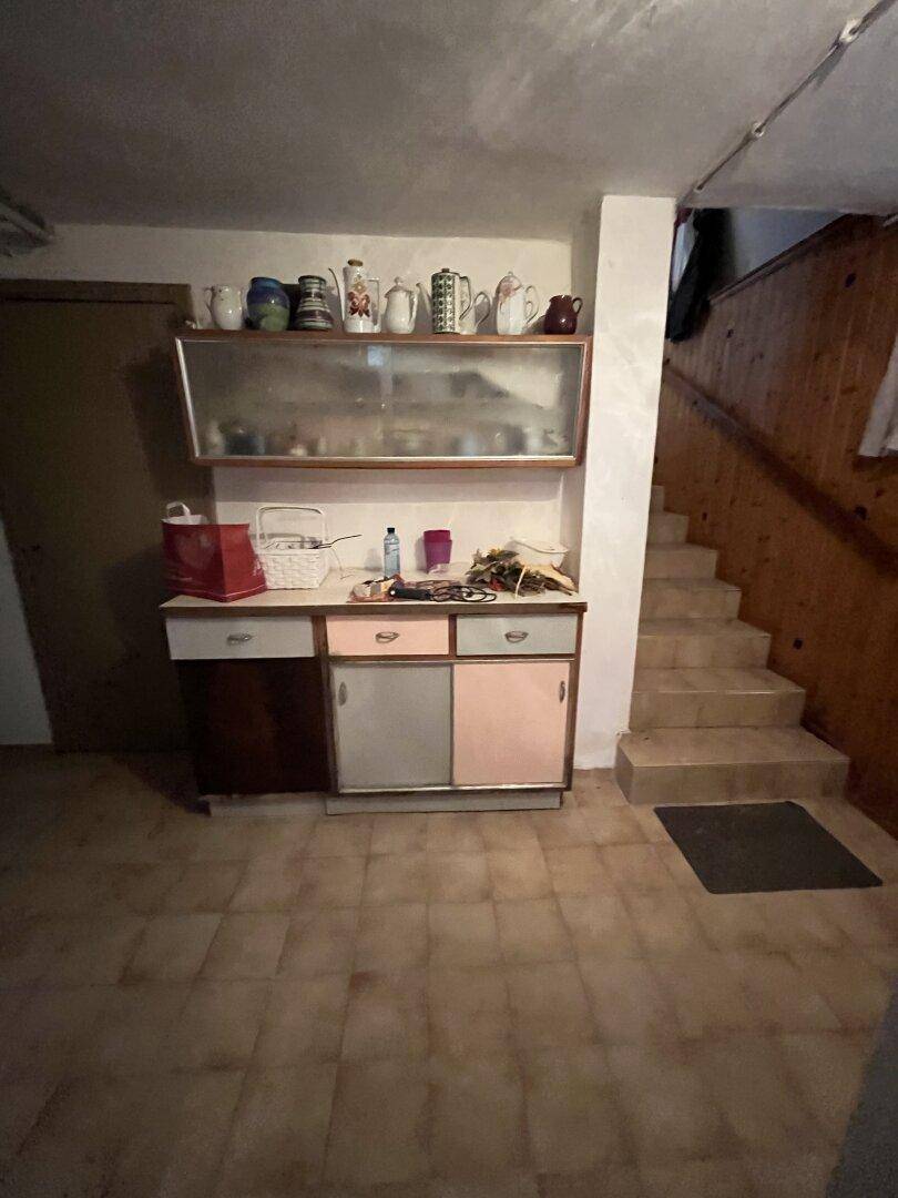 Kellerraum mit altem Schrank, Fliesenboden und Treppe, die in ein höheres Stockwerk führt.