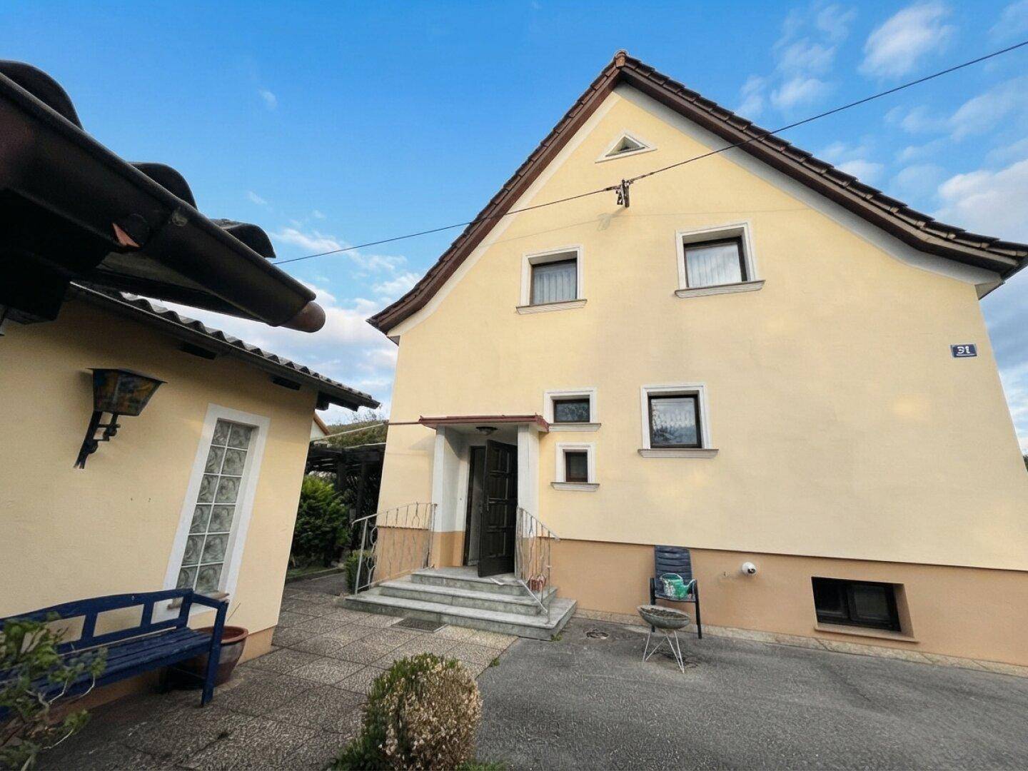 Eingangsbereich des Hauses mit Treppe und kleiner Veranda, umgeben von einem gepflegten Vorgarten.
