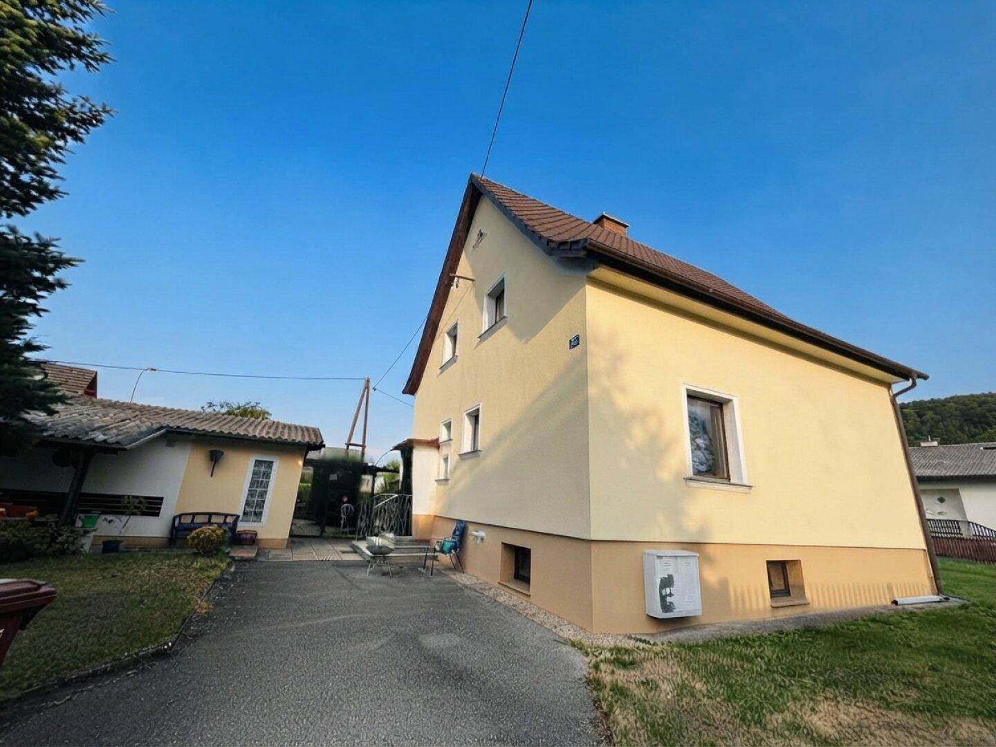Seitenansicht des Hauses mit Zufahrt und einem Nebengebäude im ländlichen Stil.