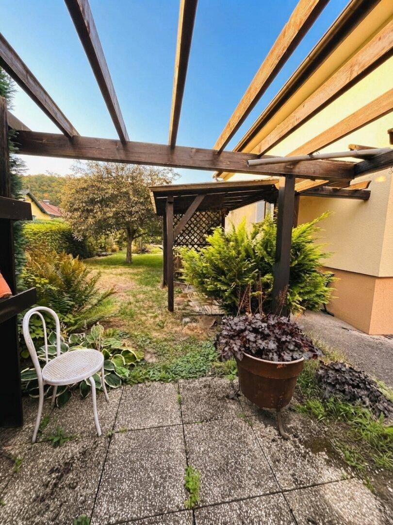 Gepflegter Gartenbereich mit einer Holzpergola und einem Steinplattenweg, umgeben von Pflanzen.