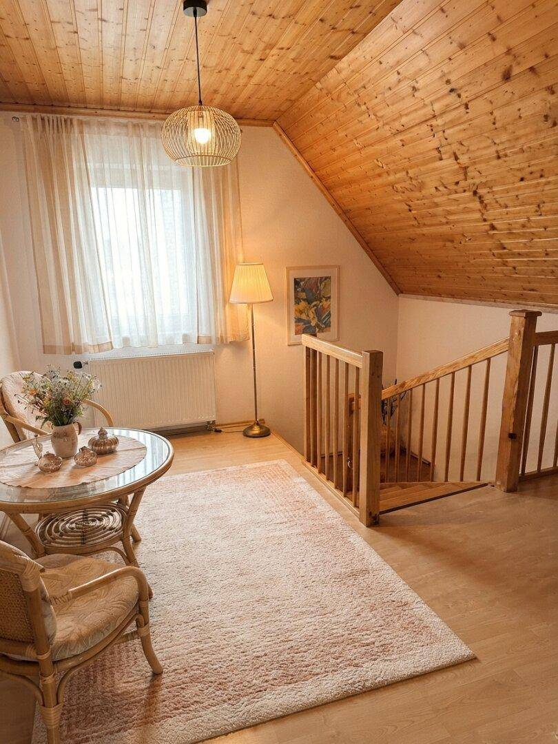 Heller Treppenabsatz mit Holzgeländer, schräger Holzdecke und Fenster, einladend gestaltet.