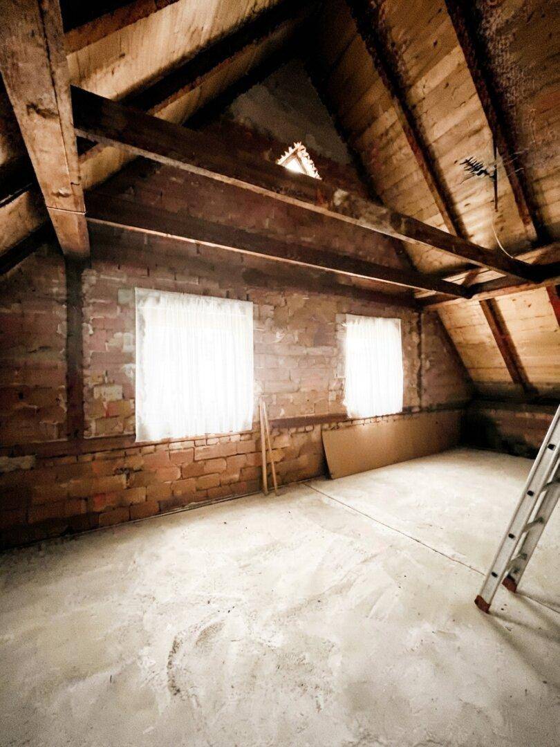 Unausgebauter Dachboden mit sichtbaren Holzbalken und Ziegelwänden, bereit für den Ausbau.