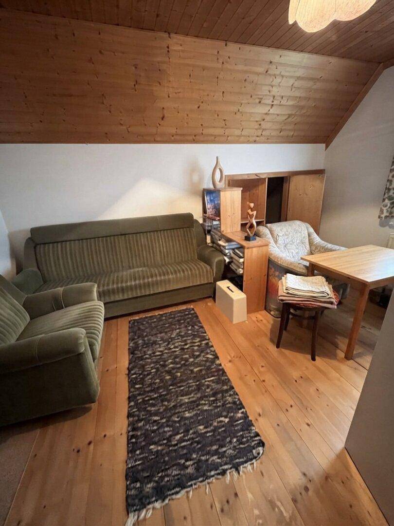 Dachzimmer mit schräger Holzdecke, Holzboden und einfacher Einrichtung, bietet viel Potenzial.