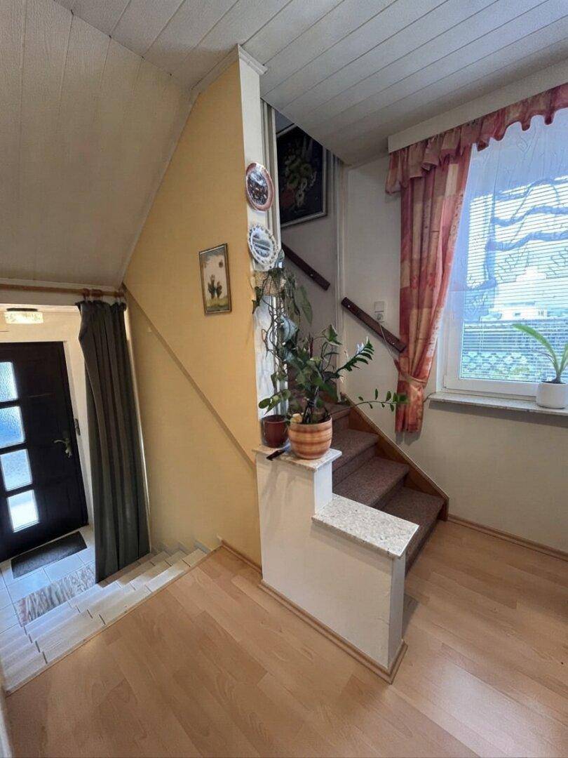 Eingangsbereich mit Treppe, Holzboden und Fenster, hell und funktional gestaltet.