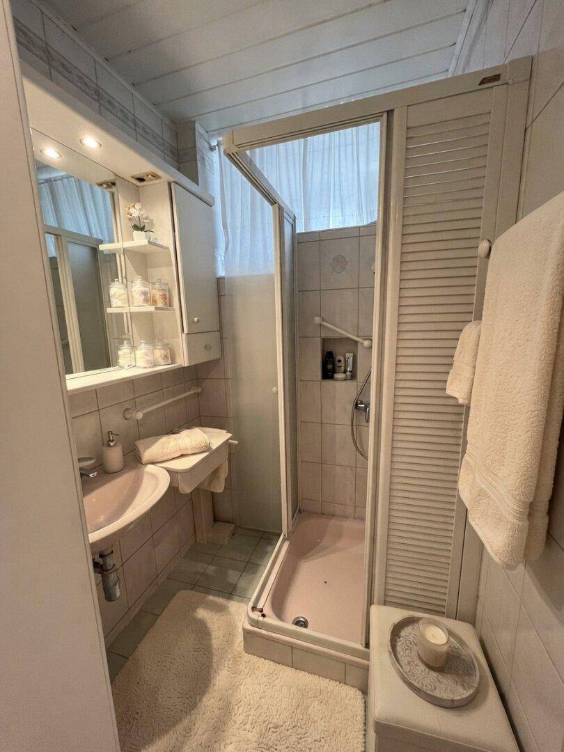 Kleines Badezimmer mit Dusche, rosa Waschbecken und hellen Fliesen, funktional und gepflegt.