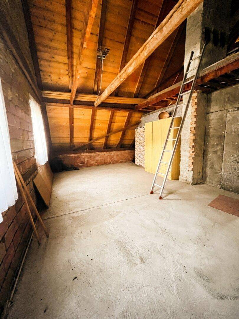 Unausgebauter Dachboden mit sichtbaren Holzbalken und Betonboden, bietet Ausbaupotenzial.