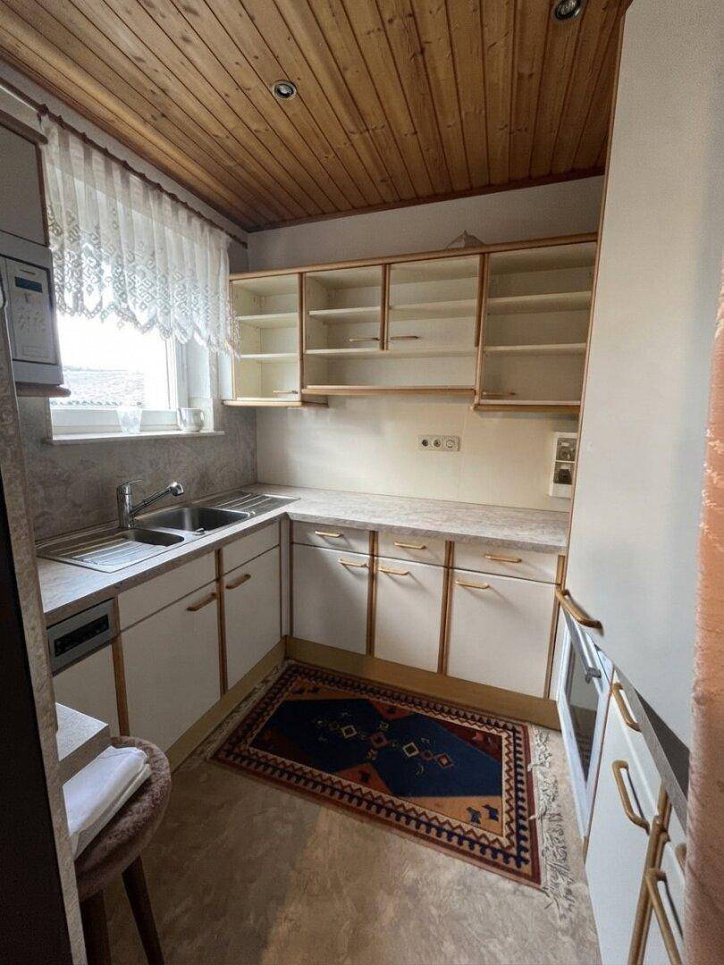 Kleine Küche mit Holzdecke, weißen Schränken und Spülbecken unter einem Fenster.