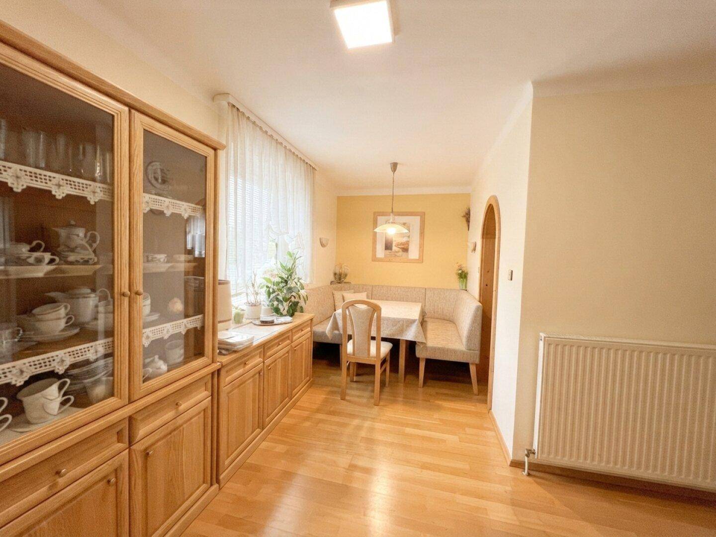 Heller Essbereich mit Eckbank, Holzboden und einem großen Vitrinenschrank.