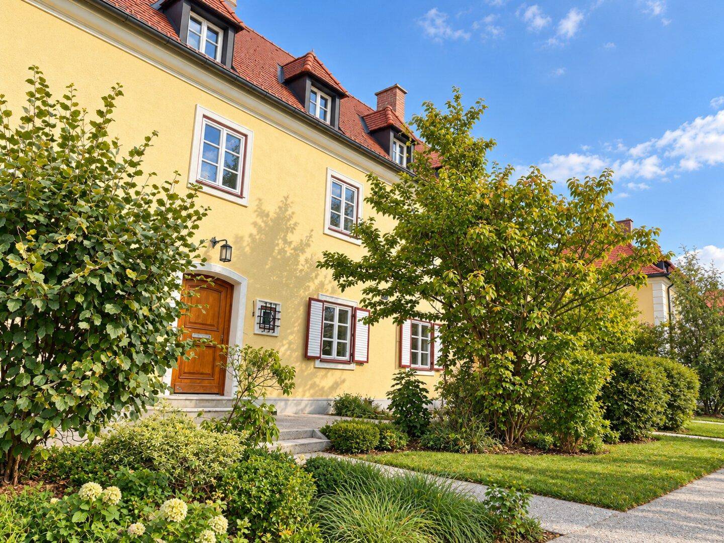 Detailansicht der gelben Fassade mit Holztür, weißen Fenstern und gepflegtem Vorgarten.