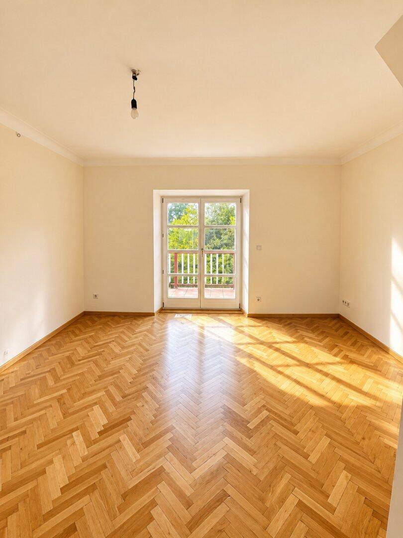 Helles Wohnzimmer mit Fischgrätparkett und Zugang zu einem kleinen Balkon.