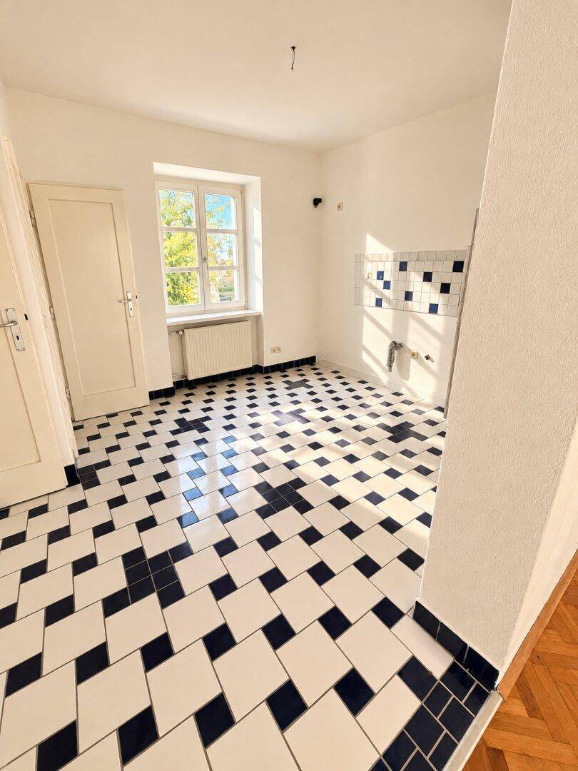 Leere Küche mit auffälligem schwarz-weißem Fliesenboden und Fenster.