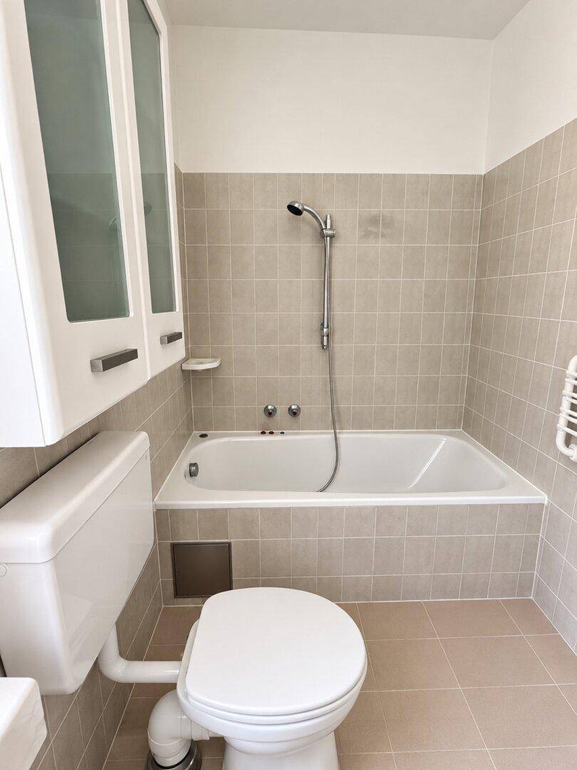 Badezimmer mit Badewanne, Toilette und beigefarbenen Fliesen an Wänden und Boden.