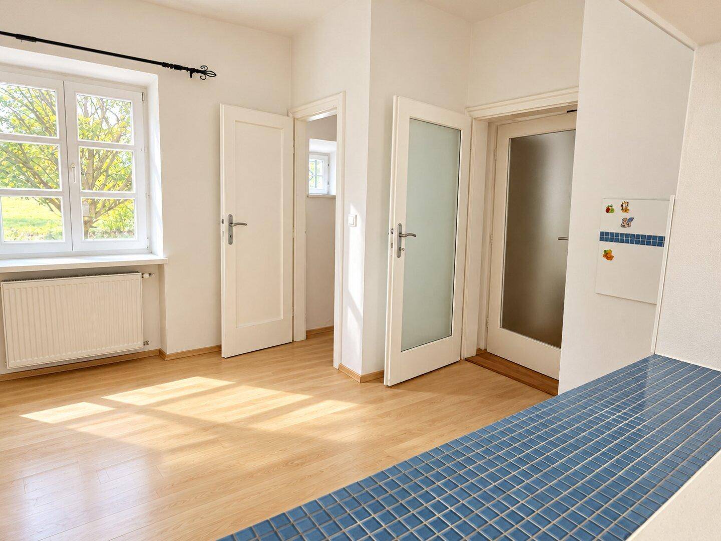 Heller Raum mit Laminatboden, Fenster und einer gefliesten Ablagefläche.