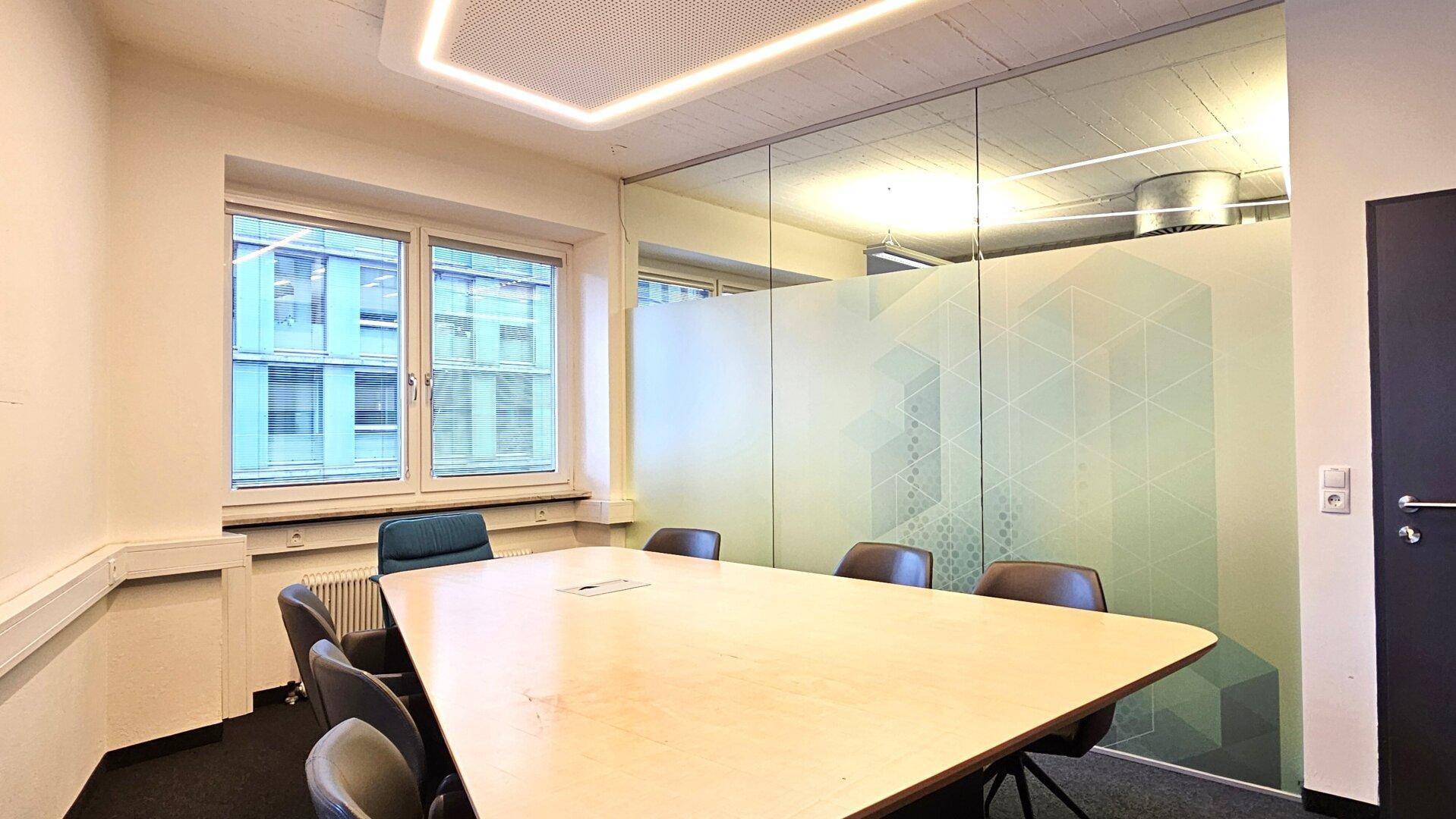 Moderner Konferenzraum mit großem Holztisch, bequemen Stühlen und Fensterblick in einem Bürogebäude.