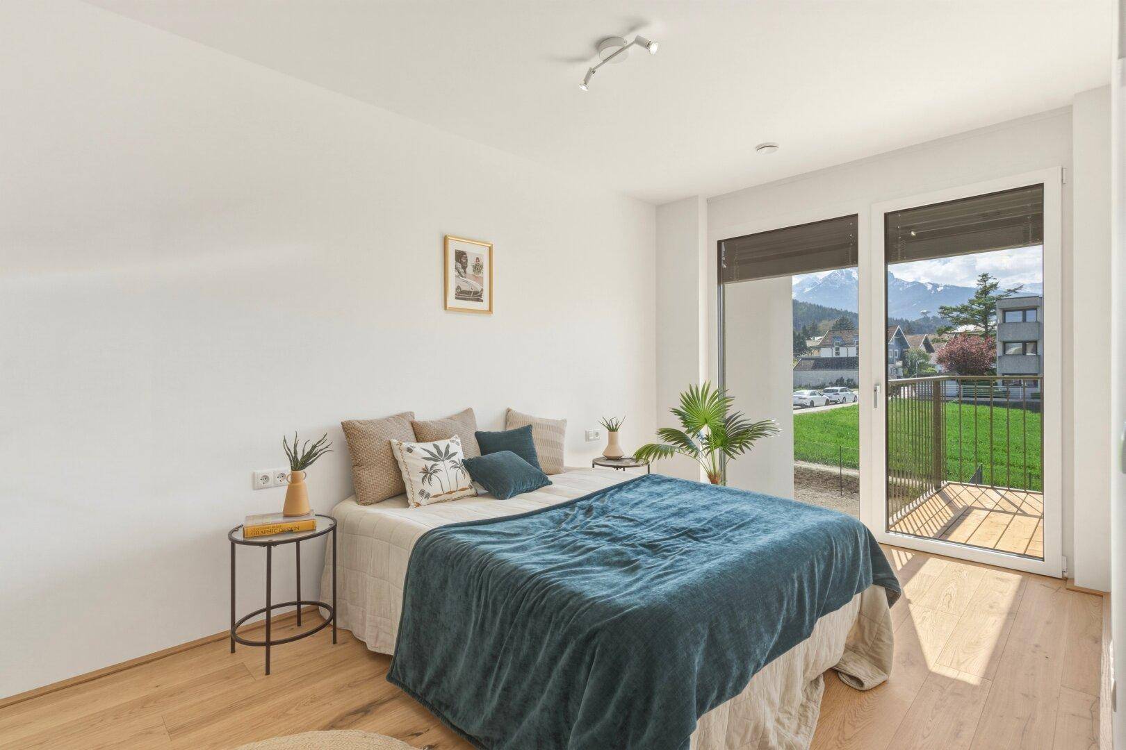Helles Schlafzimmer mit Holzboden, Balkonzugang und Blick auf die Berge.